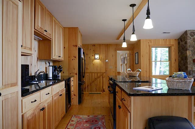Detailed view of the cabin kitchen featuring natural pine cabinets, long black countertops, a central island, and modern pendant lights.
