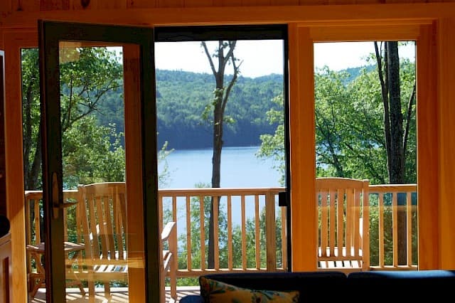 Stunning lake and forest view seen through open glass doors. The private deck and railing frame a serene lakefront landscape.