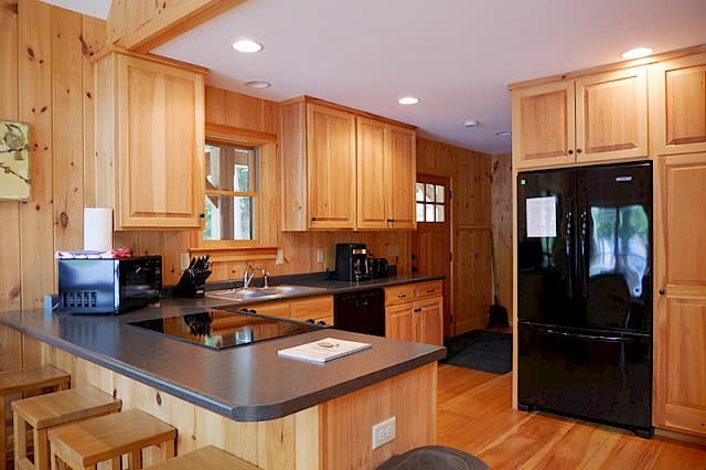 Fully equipped cabin kitchen featuring knotty pine walls and cabinets. Includes a large black fridge, modern cooktop, and a peninsula breakfast bar with stools.