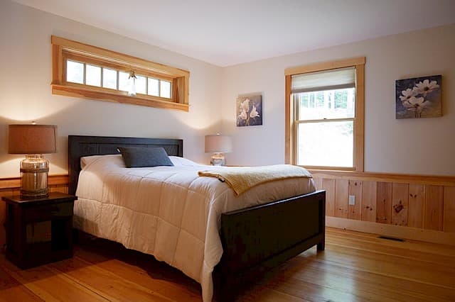 Inviting queen bedroom with a dark wood bed frame and nightstands. Features warm pine wainscoting, wood floors, and a unique transom window above the bed.
