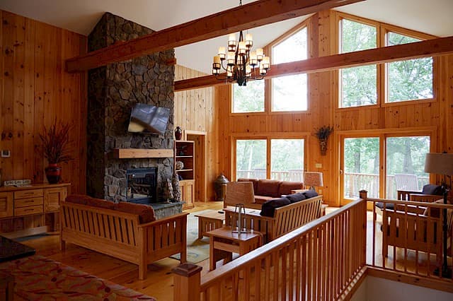 Stunning two-story great room. Features a massive stone fireplace, a soaring vaulted ceiling with beams, pine walls, and a full wall of windows overlooking the deck.