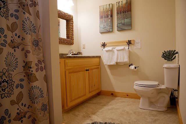 Clean, full bathroom featuring a light wood vanity, granite counter, and rustic wicker mirror. A colorful floral curtain complements the rustic wood towel rack.