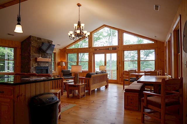 Stunning open-concept great room with a vaulted ceiling, a full wall of windows, and a stone fireplace. Features the living, dining, and kitchen bar areas.