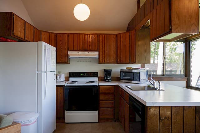 A cabin kitchen with a vaulted ceiling, dark wood cabinets, a white fridge, a black stove, and white countertops with a sink.