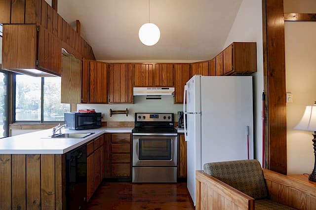 A cabin kitchen with a vaulted ceiling, wood paneling and cabinets, a white fridge, and a stainless steel and black range.