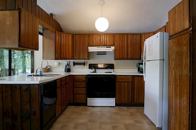 A cabin kitchen with dark wood cabinets, a white fridge, a black stove, white countertops, and a single globe pendant light.