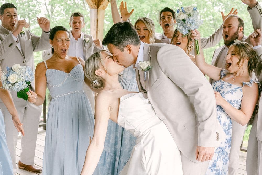A joyful wedding party celebrates as the couple shares a kiss.