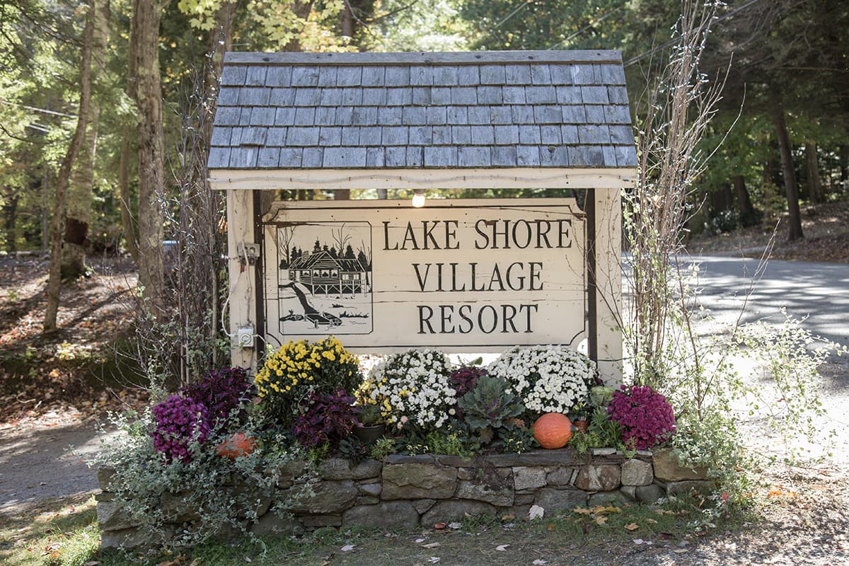 Sign for Lake Shore Village Resort surrounded by colorful flowers and autumn foliage.