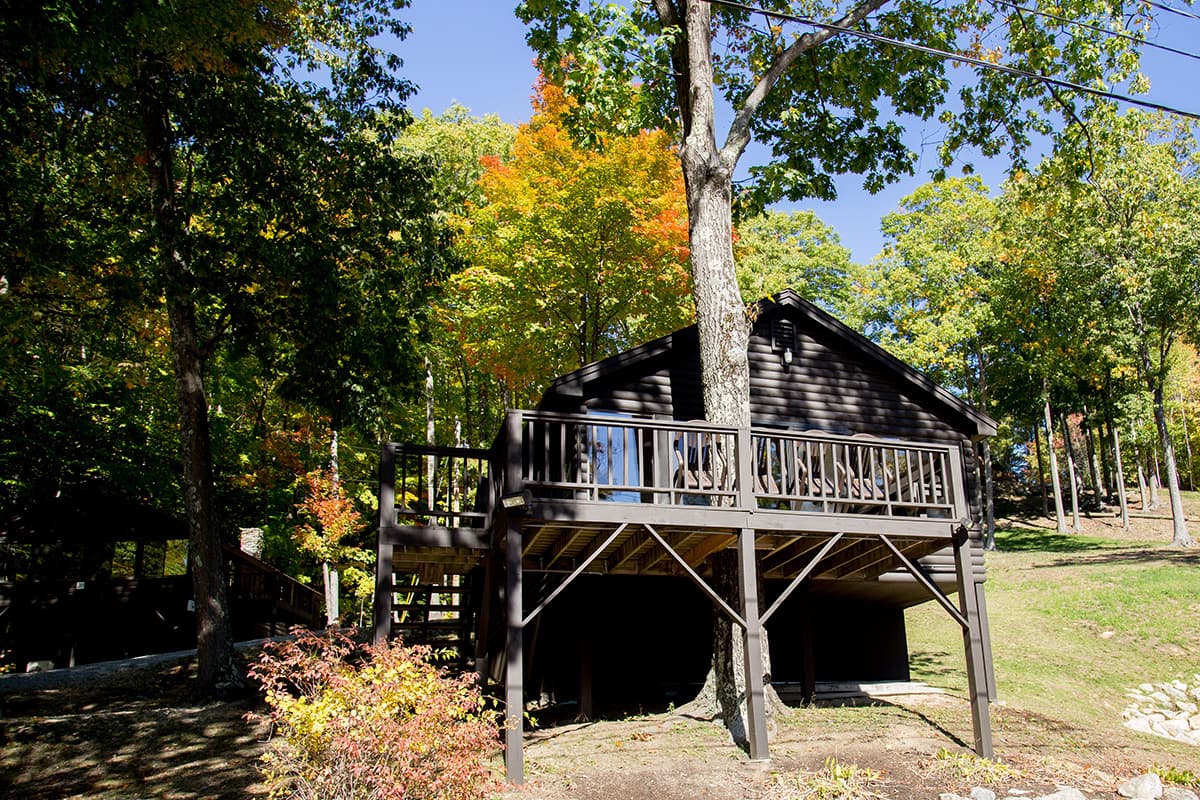 Wooden cabin elevated on stilts, surrounded by vibrant autumn foliage.