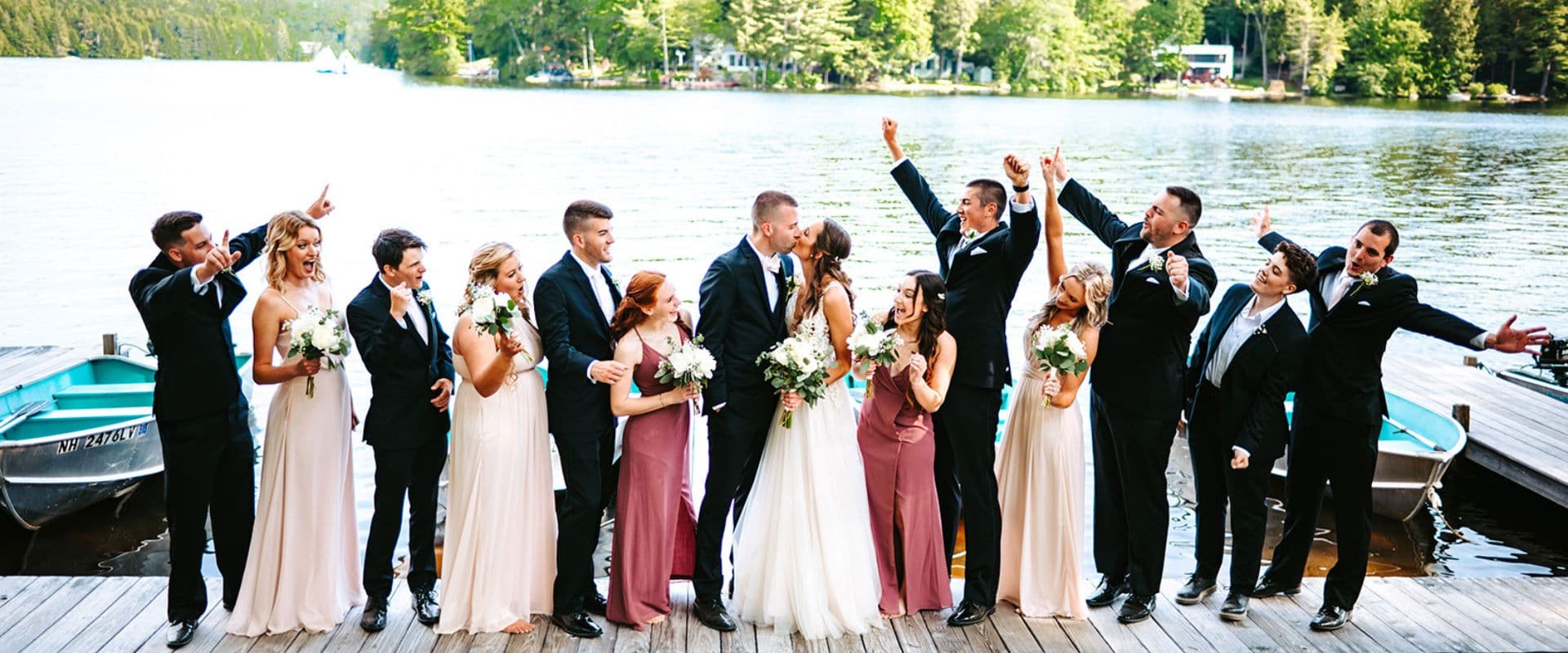 A joyful wedding party poses together on a dock by a lake, celebrating with flowers and smiles. A joyful wedding party poses together on a dock by a lake, celebrating with flowers and smiles.