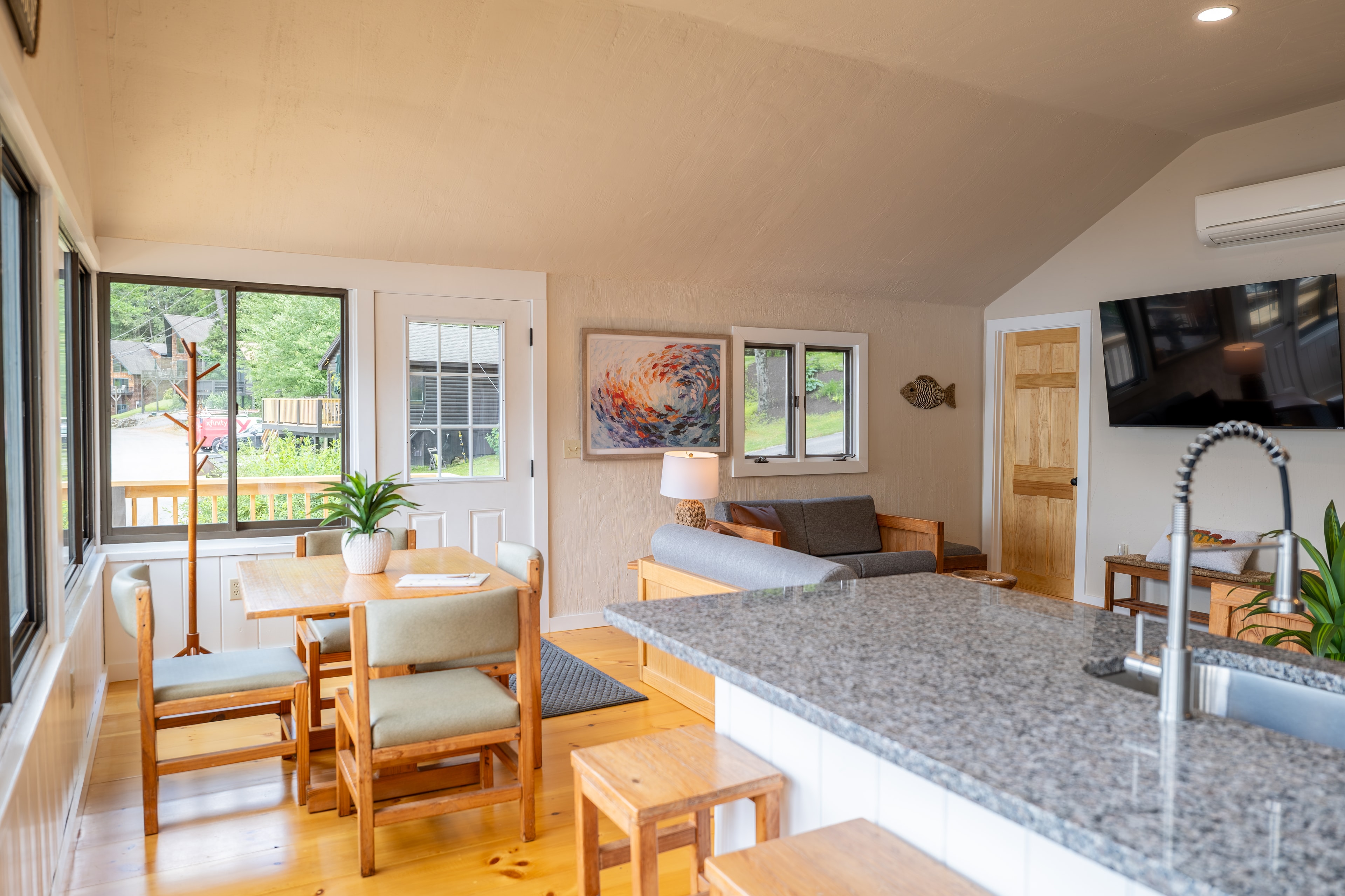 A cozy open-plan living space featuring a kitchen island, dining area, and seating with large windows.