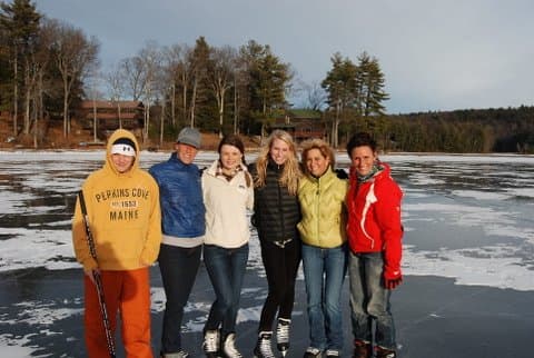 A group of six friends posing on a frozen lake, dressed in winter clothing.