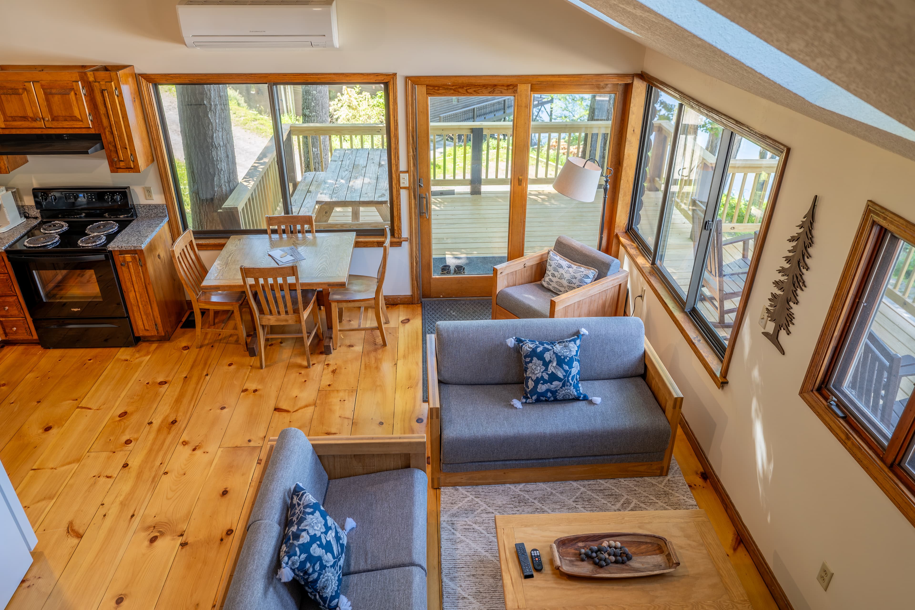 A bright cabin great room with a vaulted ceiling, hardwood floors, an open kitchen, and a sunlit living area with glass doors.