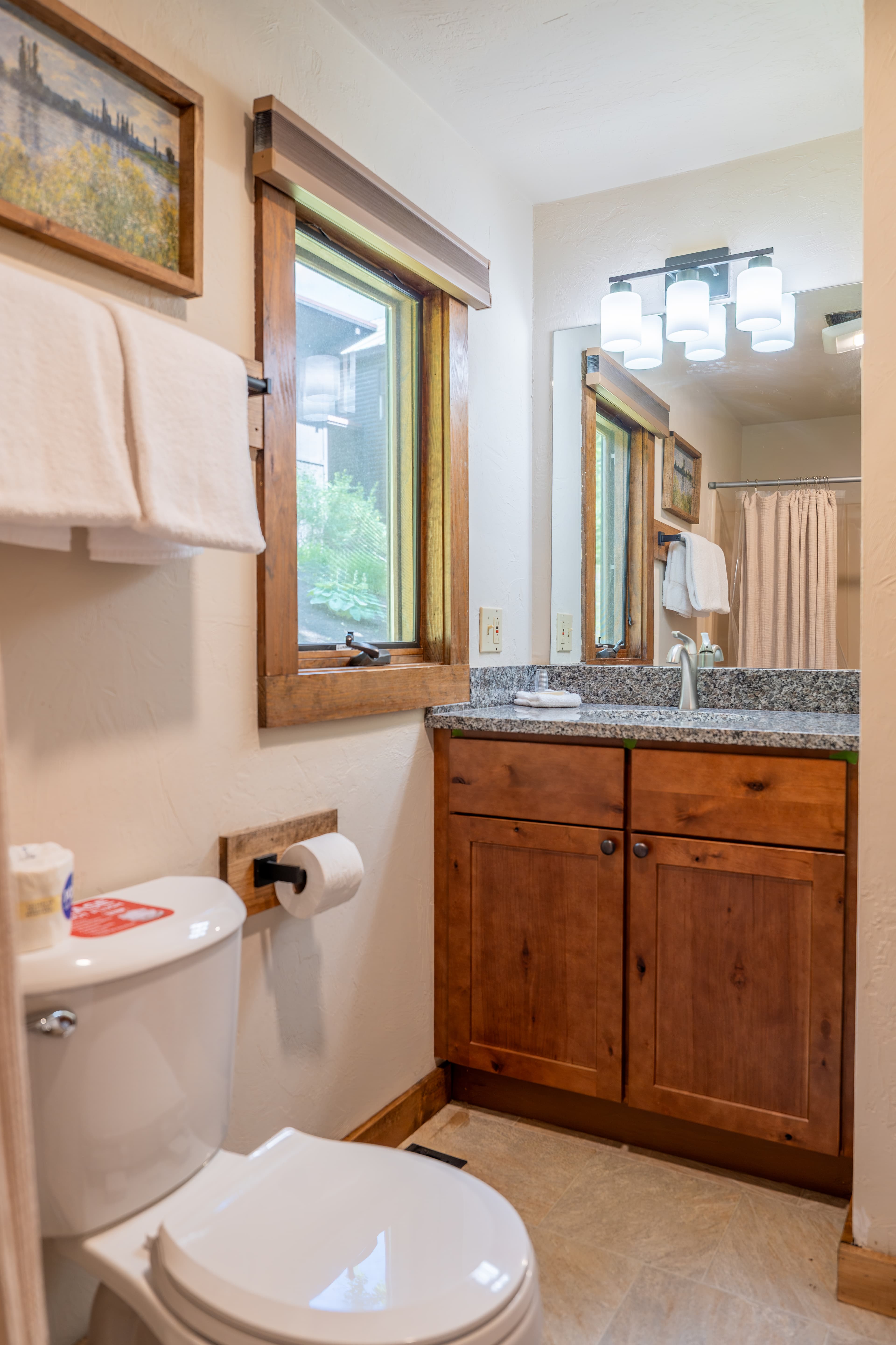 A simple bathroom scene featuring a white toilet with stacked towels, two towels on a rack, a toilet paper dispenser, and a small window.