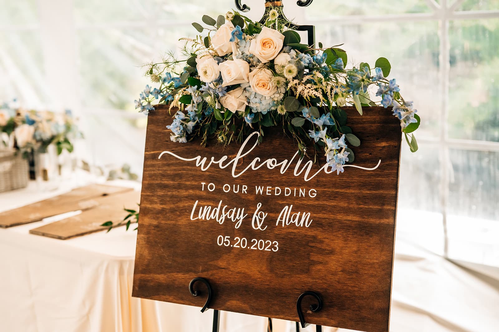 Wooden wedding welcome sign adorned with flowers, featuring the names Lindsay and Alan and the date 05.20.2023.