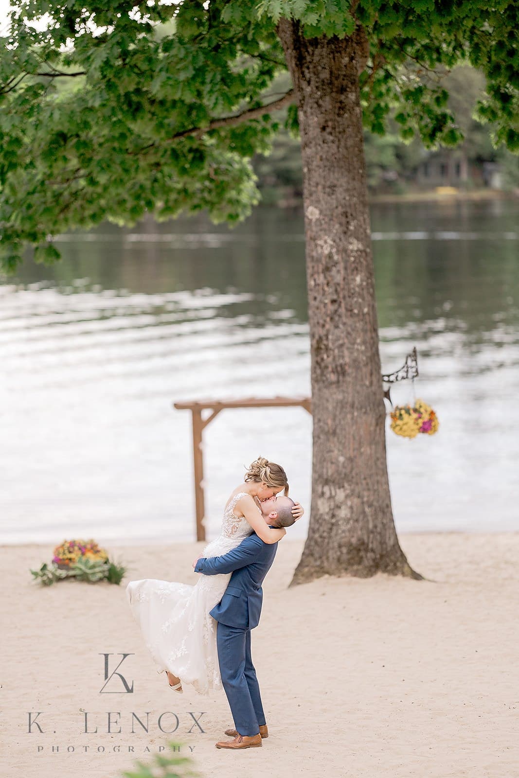 A couple celebrates their wedding by embracing on the beach near a calm lake.