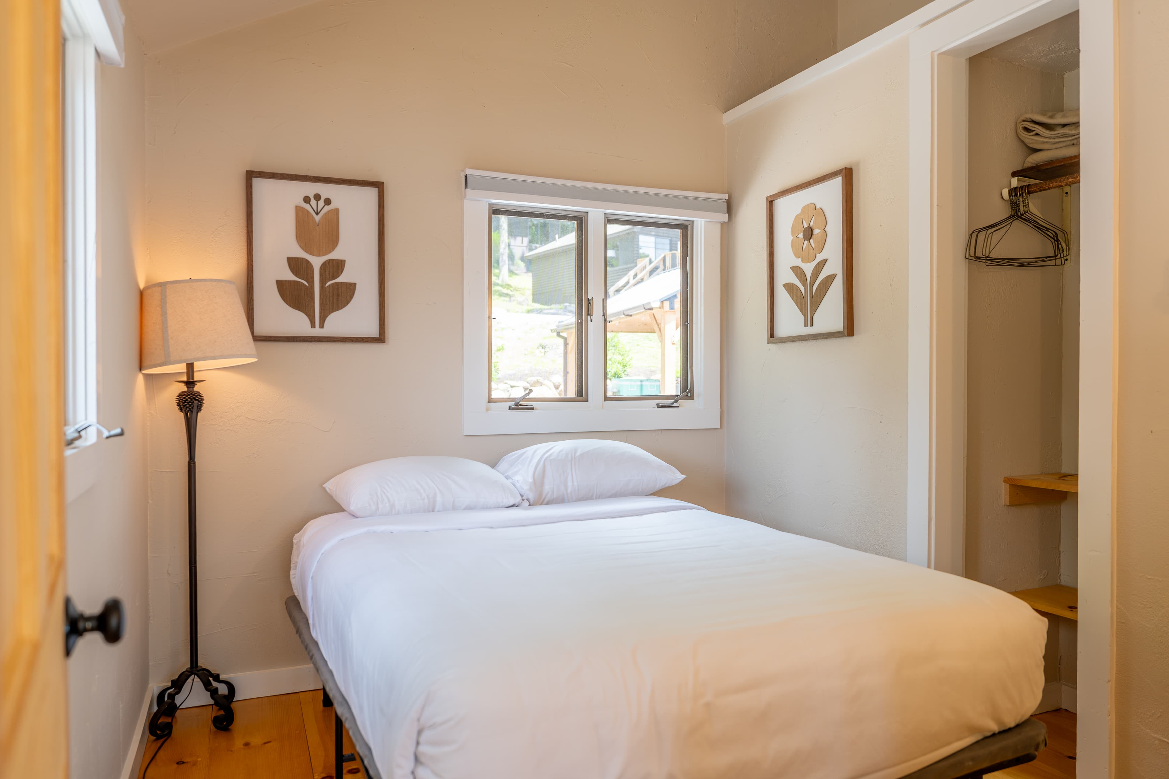 A cozy cabin bedroom with a vaulted ceiling, a bed with a ring-patterned quilt, and two windows with tied-back beige curtains.
