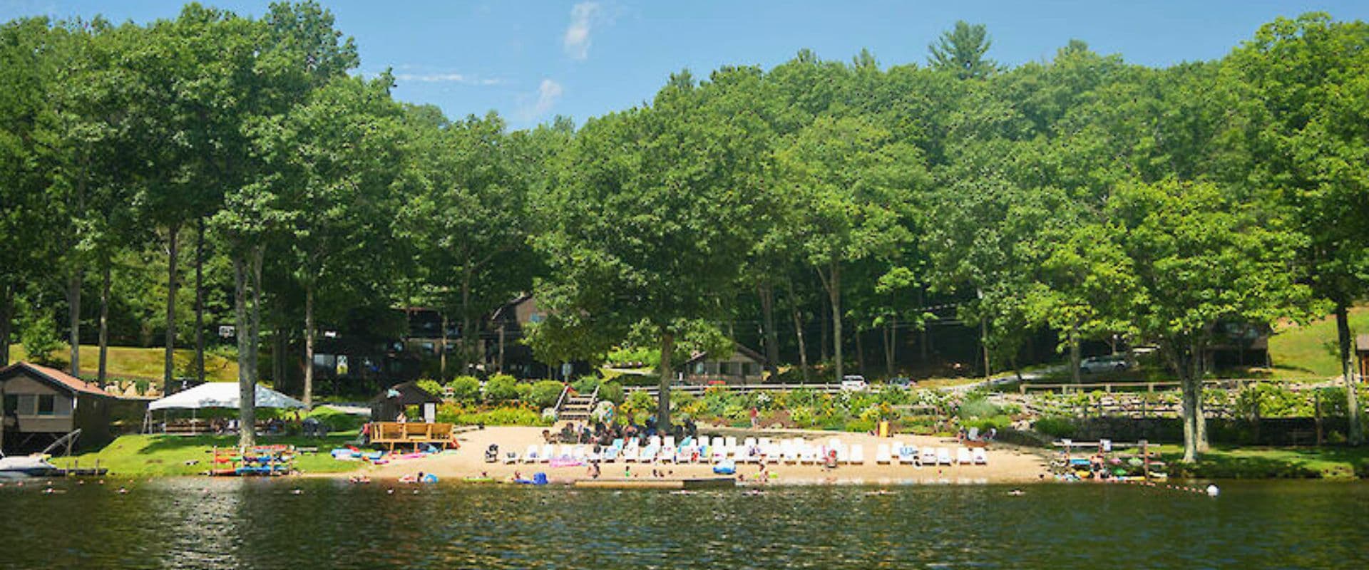 A sandy lakeshore surrounded by lush green trees and cabins.