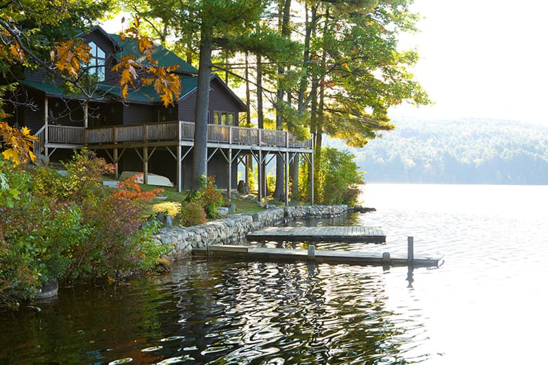 A lakeside cabin surrounded by trees and autumn foliage, with a wooden dock extending into the water.