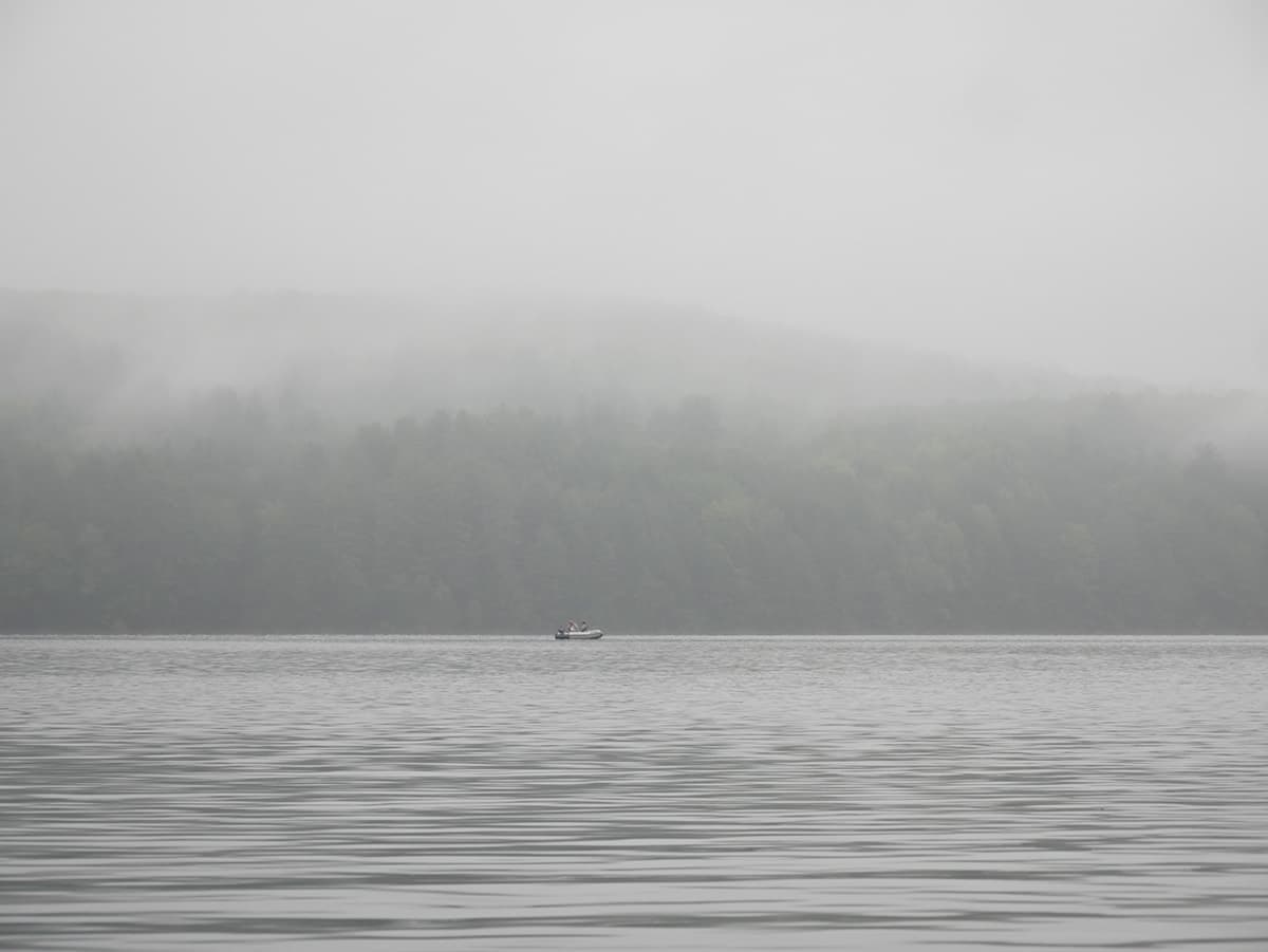 A small boat floats on a calm lake surrounded by misty forested hills.