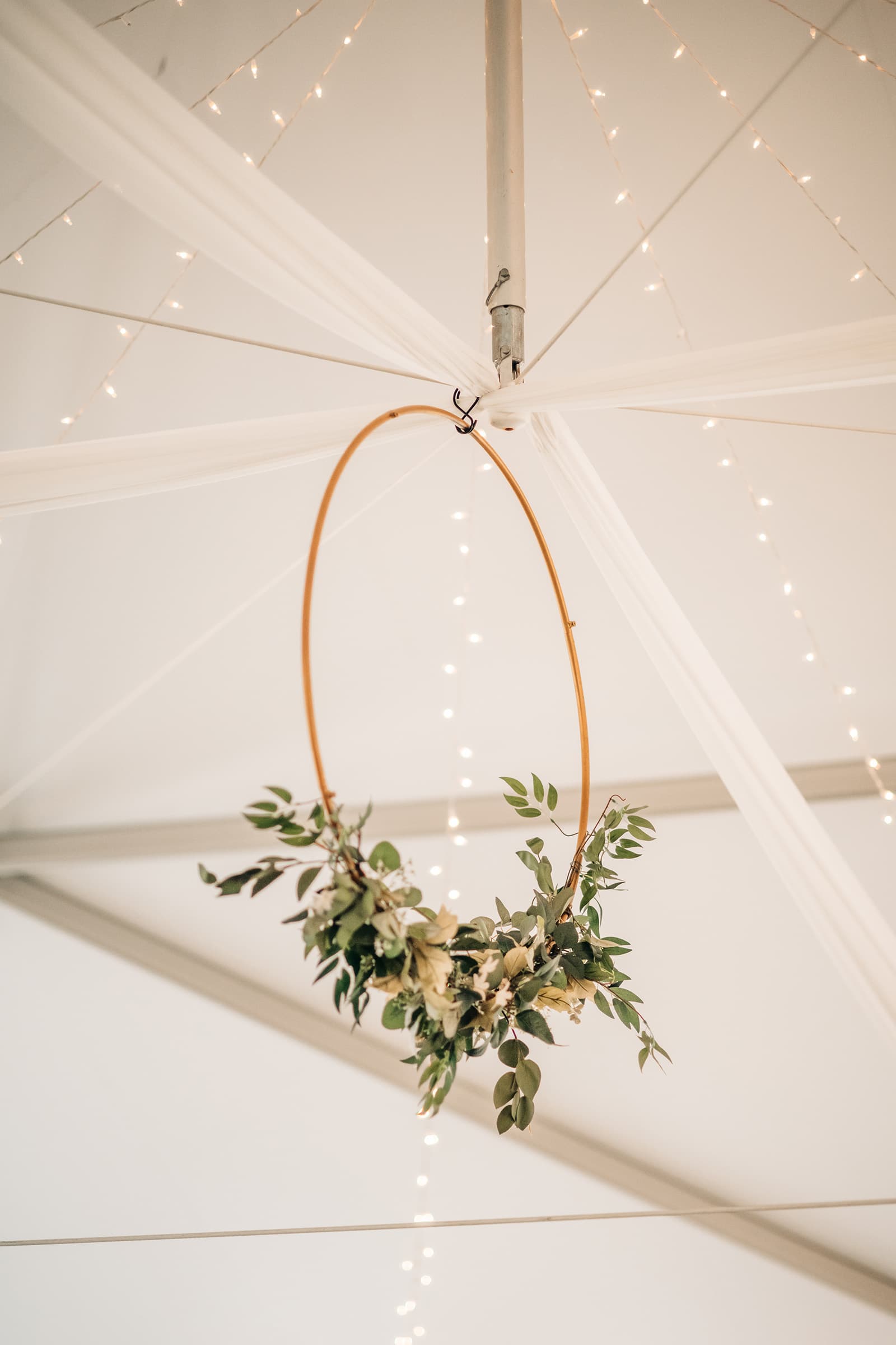 A floral hoop hangs from the ceiling beneath draped fabric and string lights.