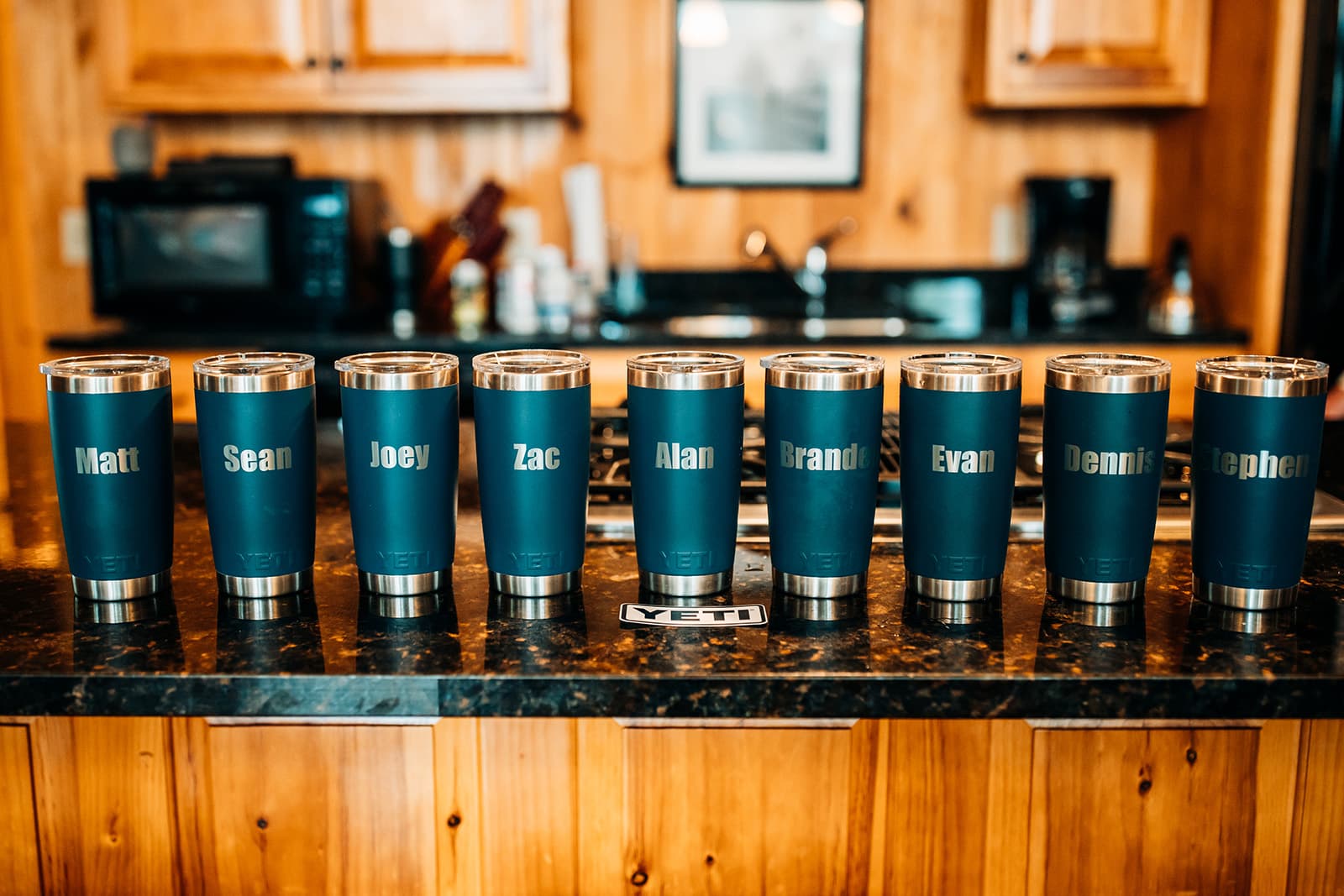 A row of personalized blue YETI tumblers with names inscribed on them, set on a counter.