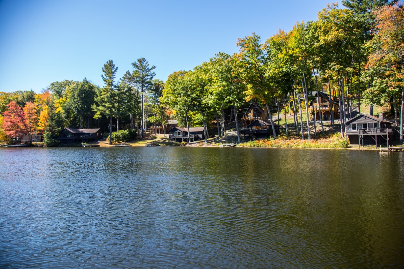 A serene lake bordered by colorful autumn trees and cozy cabins.