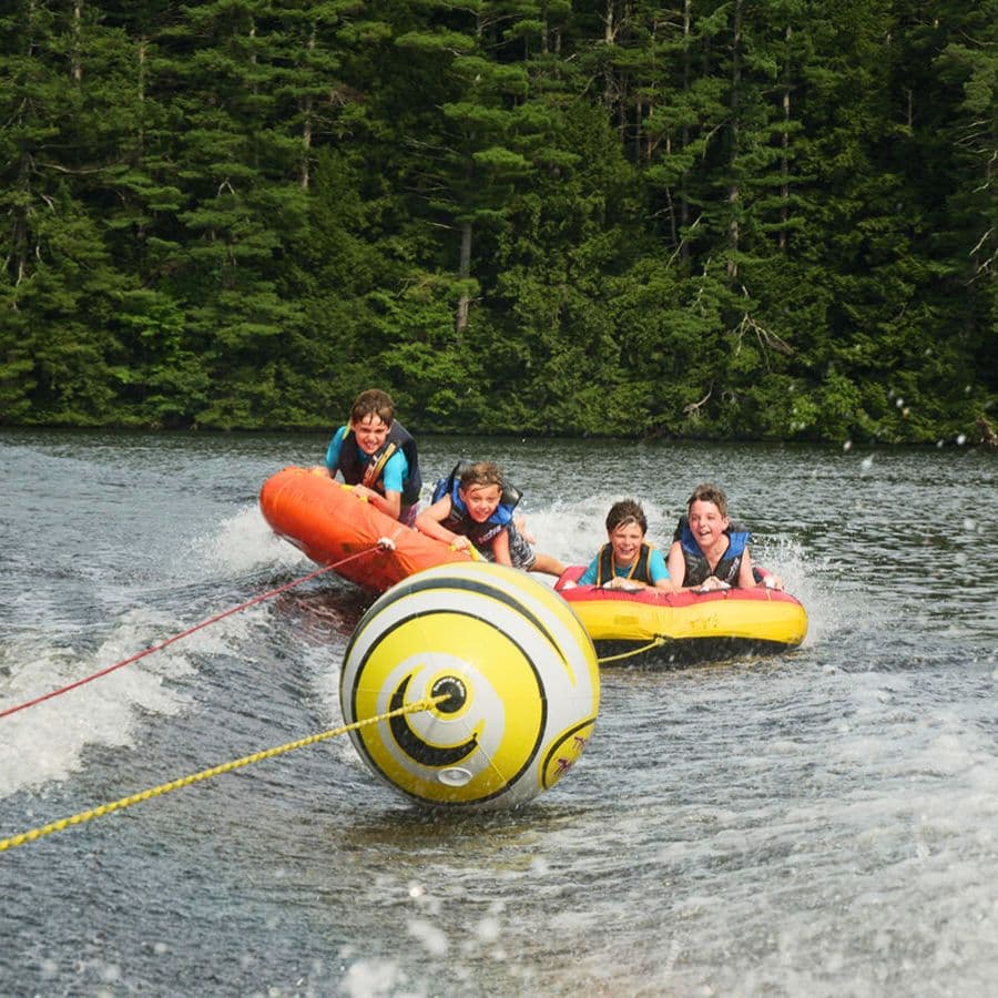 Four children enjoy tubing on a lake being pulled by a boat.