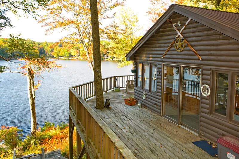 A cozy log cabin overlooks a serene lake surrounded by autumn foliage.