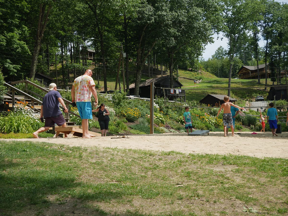 A group of children and adults engage in outdoor activities at a campground surrounded by greenery and cabins.