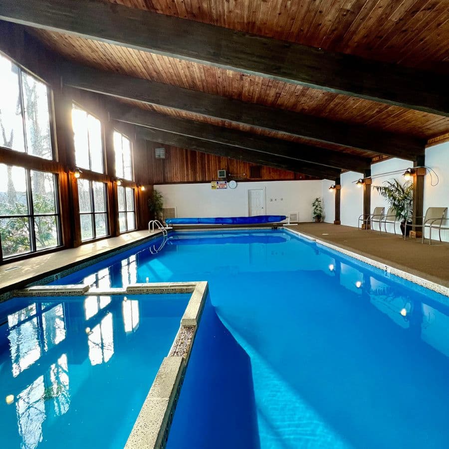 Indoor swimming pool with large windows and wood-beamed ceiling.