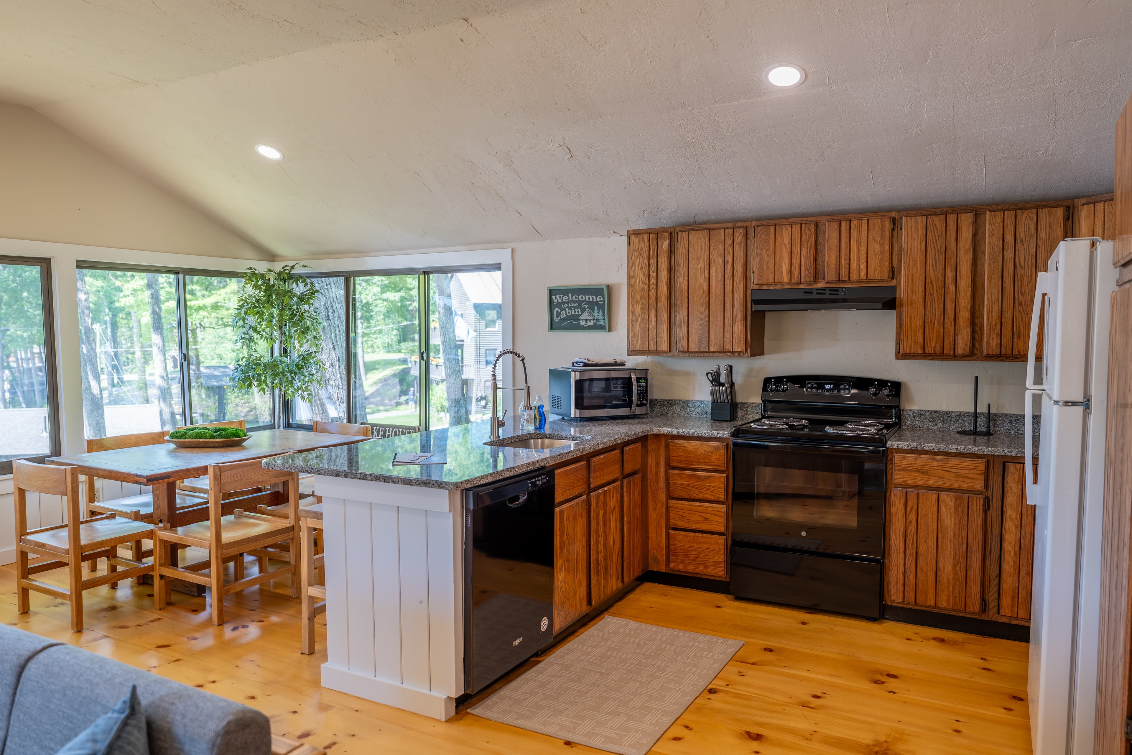 A cabin kitchen with dark wood cabinets, a white fridge, a black stove, white countertops, and a single globe pendant light.