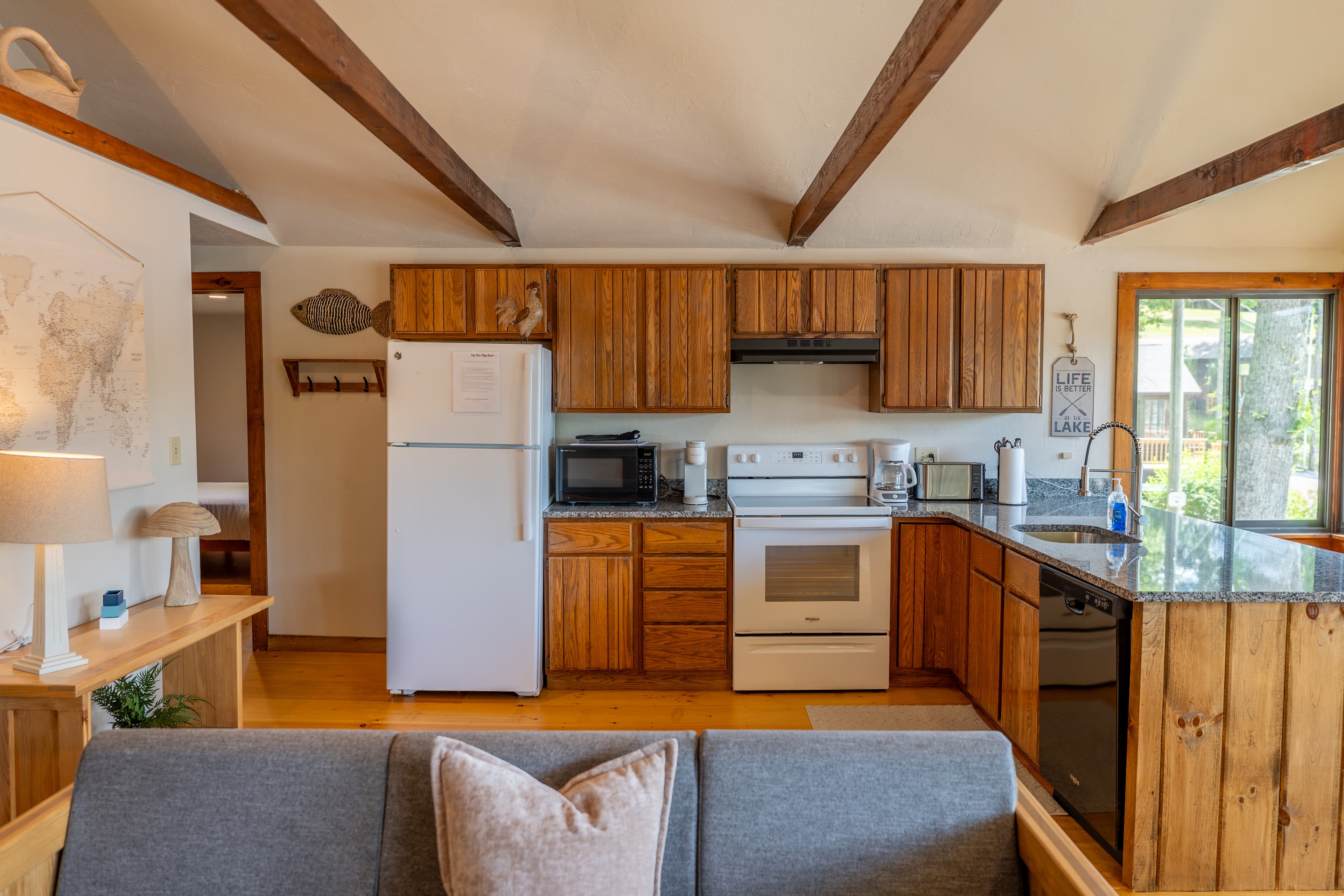 A cabin's kitchen and dining area with exposed wooden beams, featuring light wood cabinets, a white fridge, black stove, and a round wooden table.