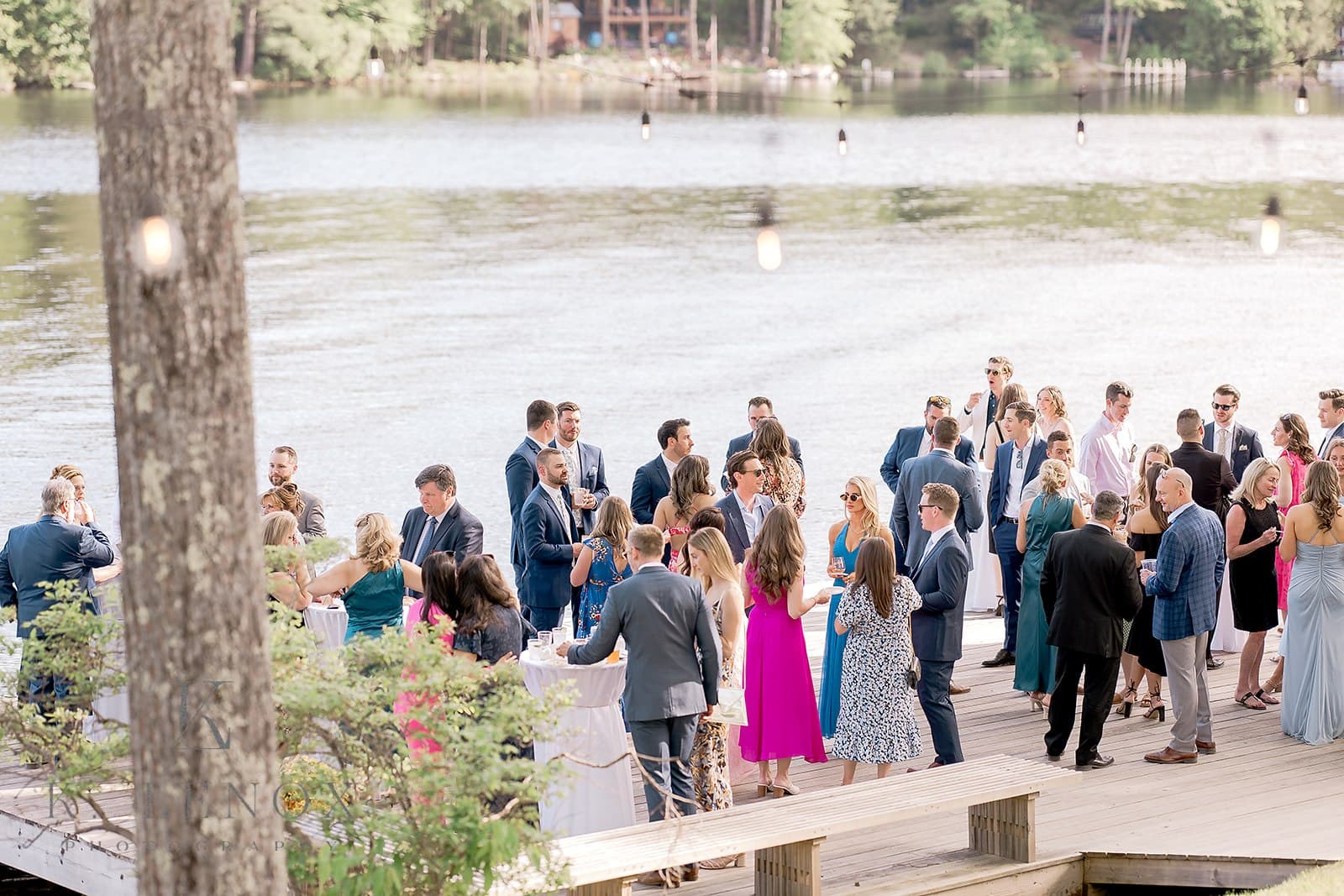 A lively outdoor gathering by the water with guests mingling and enjoying drinks.