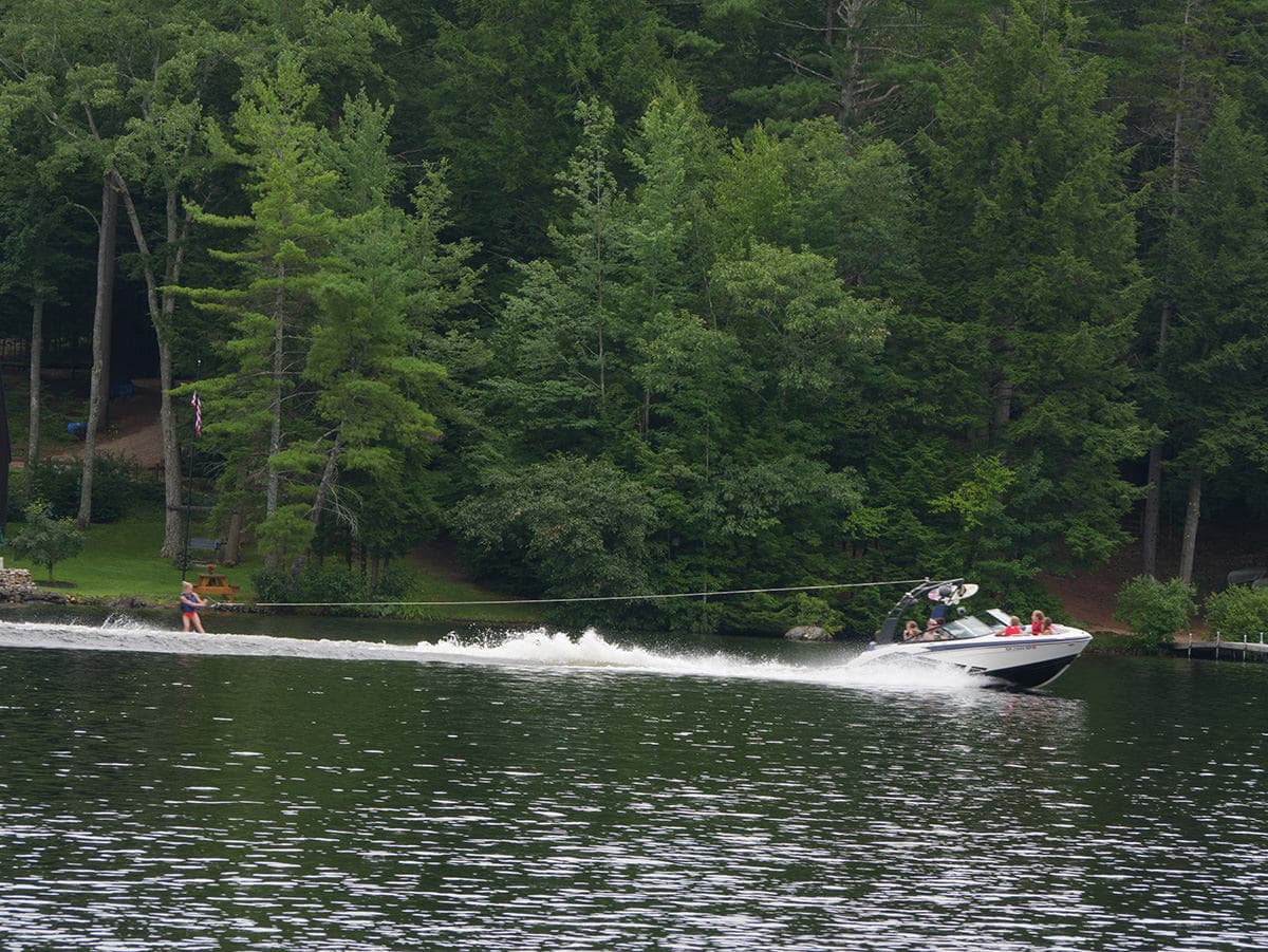 A boat pulls a person water skiing on a lake surrounded by lush greenery.