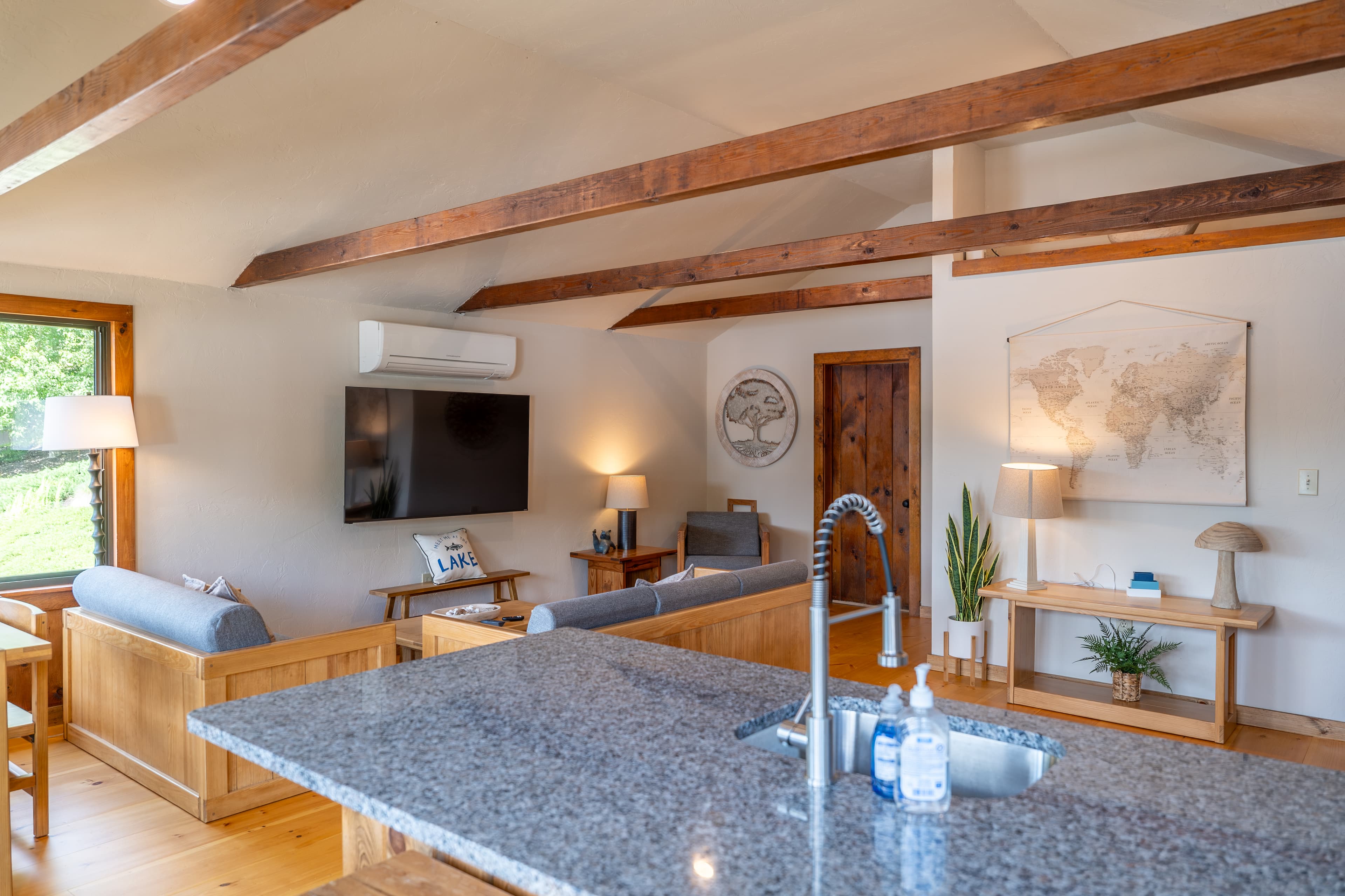 A well-lit kitchen and dining area with exposed wooden beams, modern globe lighting, wood cabinets, a white refrigerator, and a small breakfast bar.
