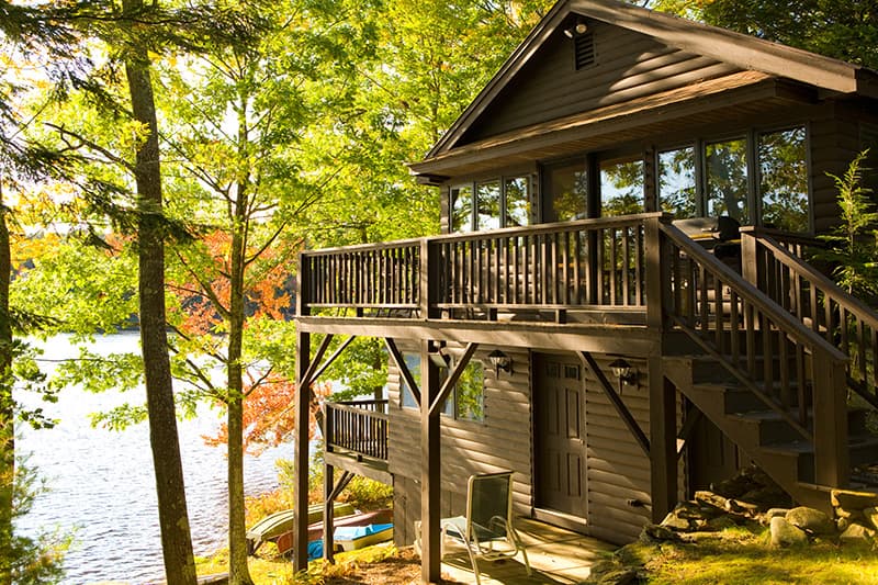 A cozy wooden cabin surrounded by lush green trees near a calm lake.
