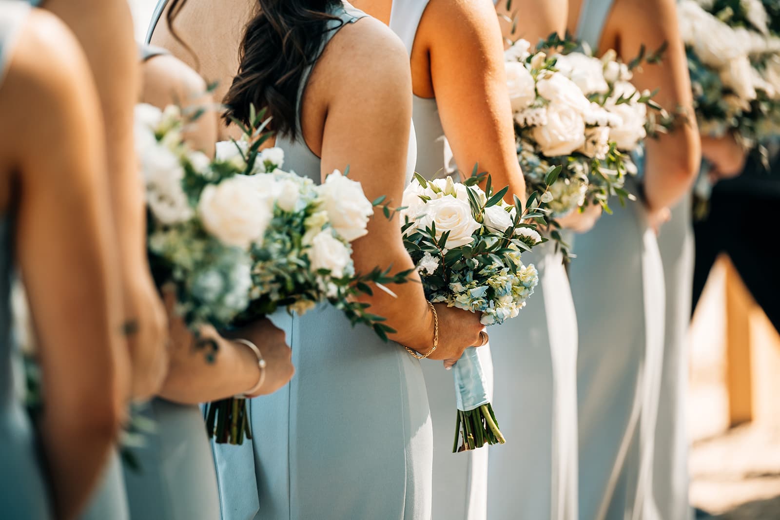 A row of bridesmaids in light blue dresses holding floral bouquets.