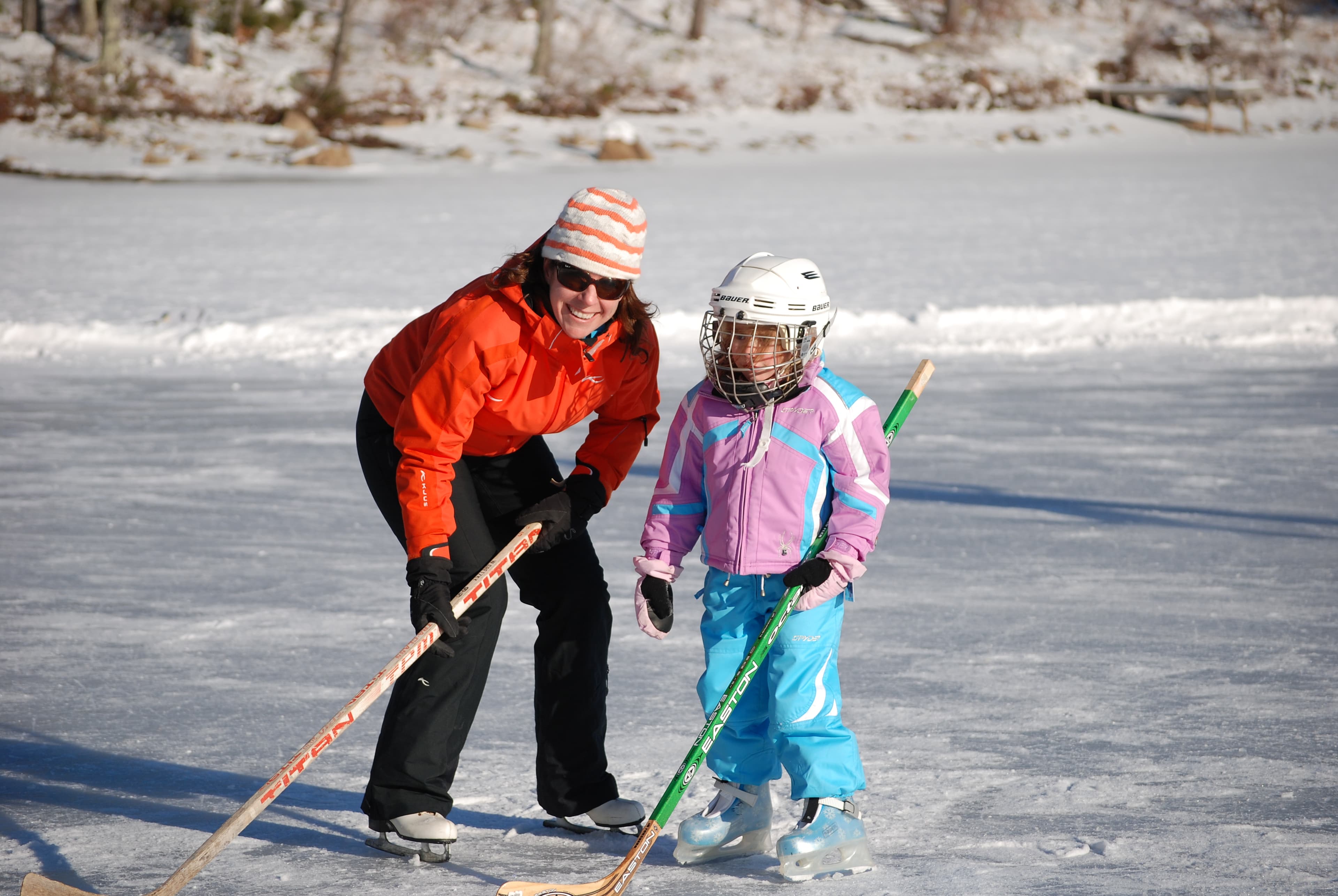 A woman and a young girl enjoy ice skating together on a frozen lake.