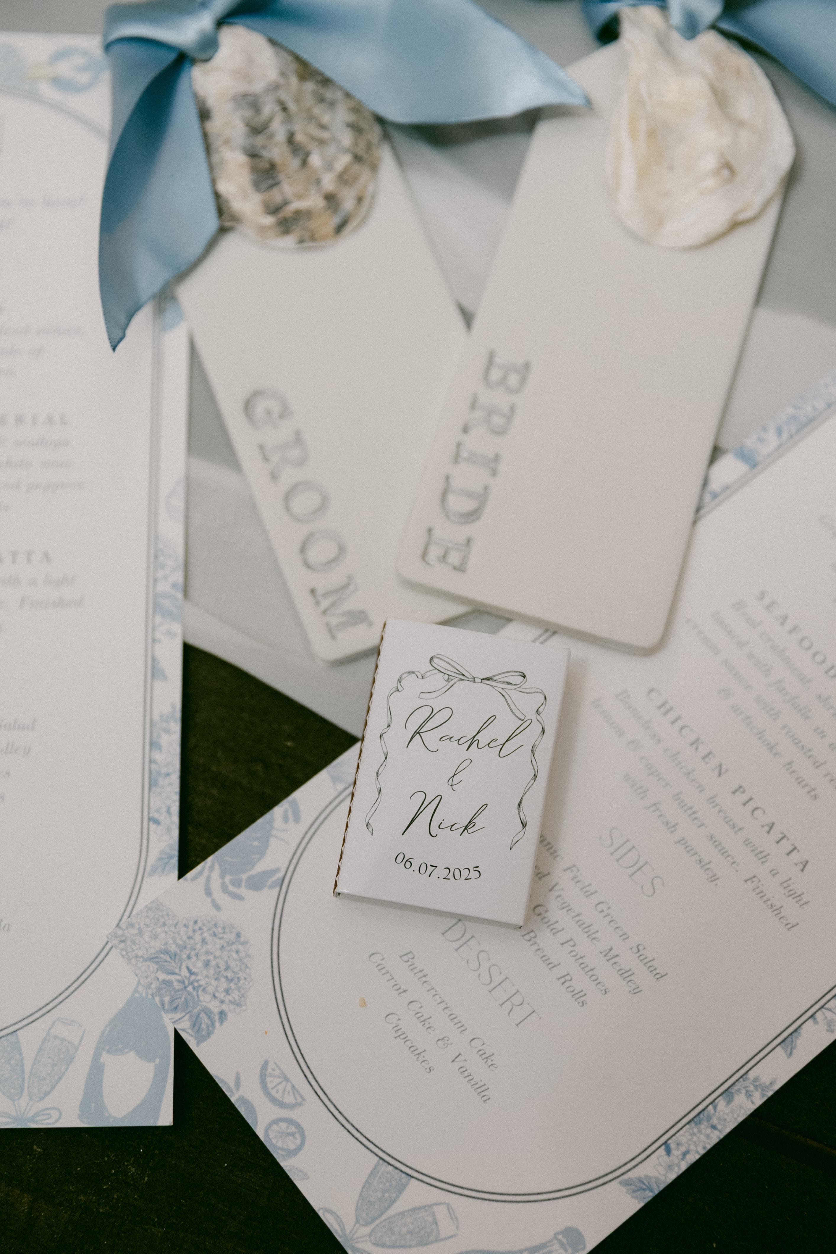 A wedding invitation suite featuring tags for the bride and groom and a menu card with a small booklet displaying the couple's names and wedding date.