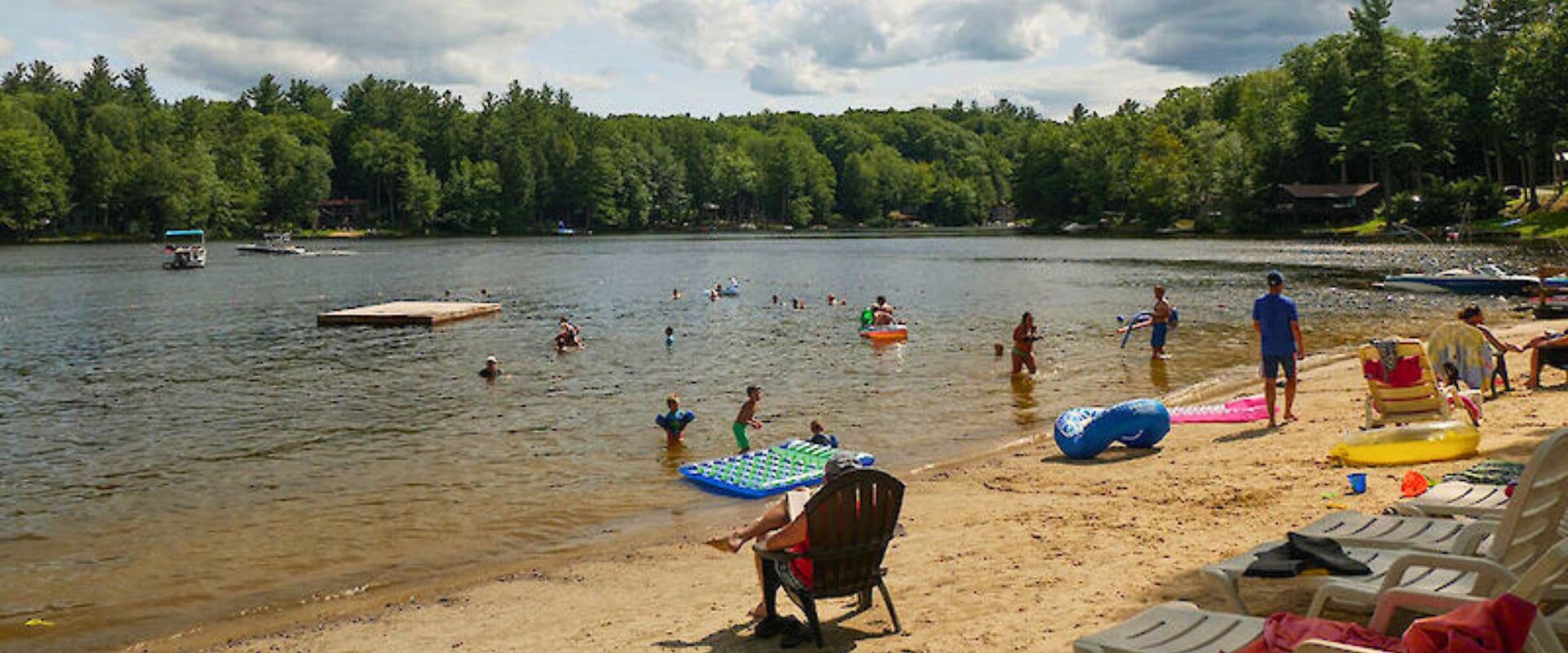 A beach scene with people swimming, floating on rafts, and relaxing on chairs along a sandy shore.