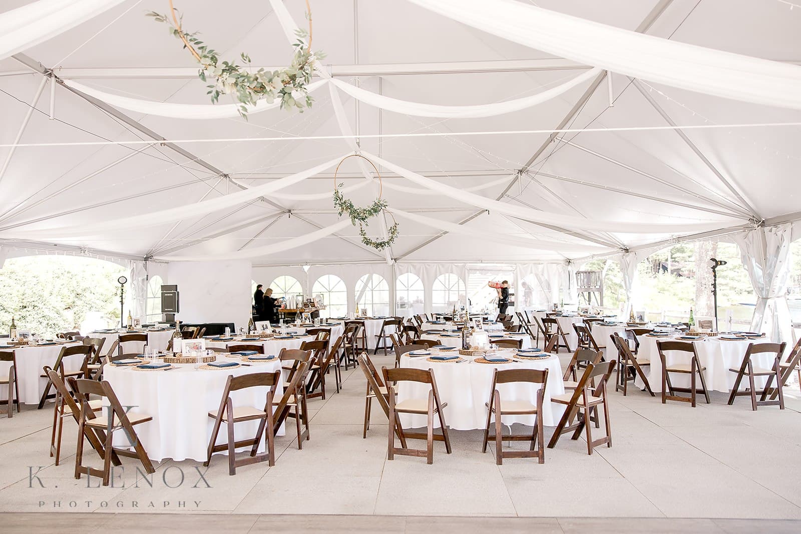 A large, elegantly decorated tent interior with round tables set for an event.