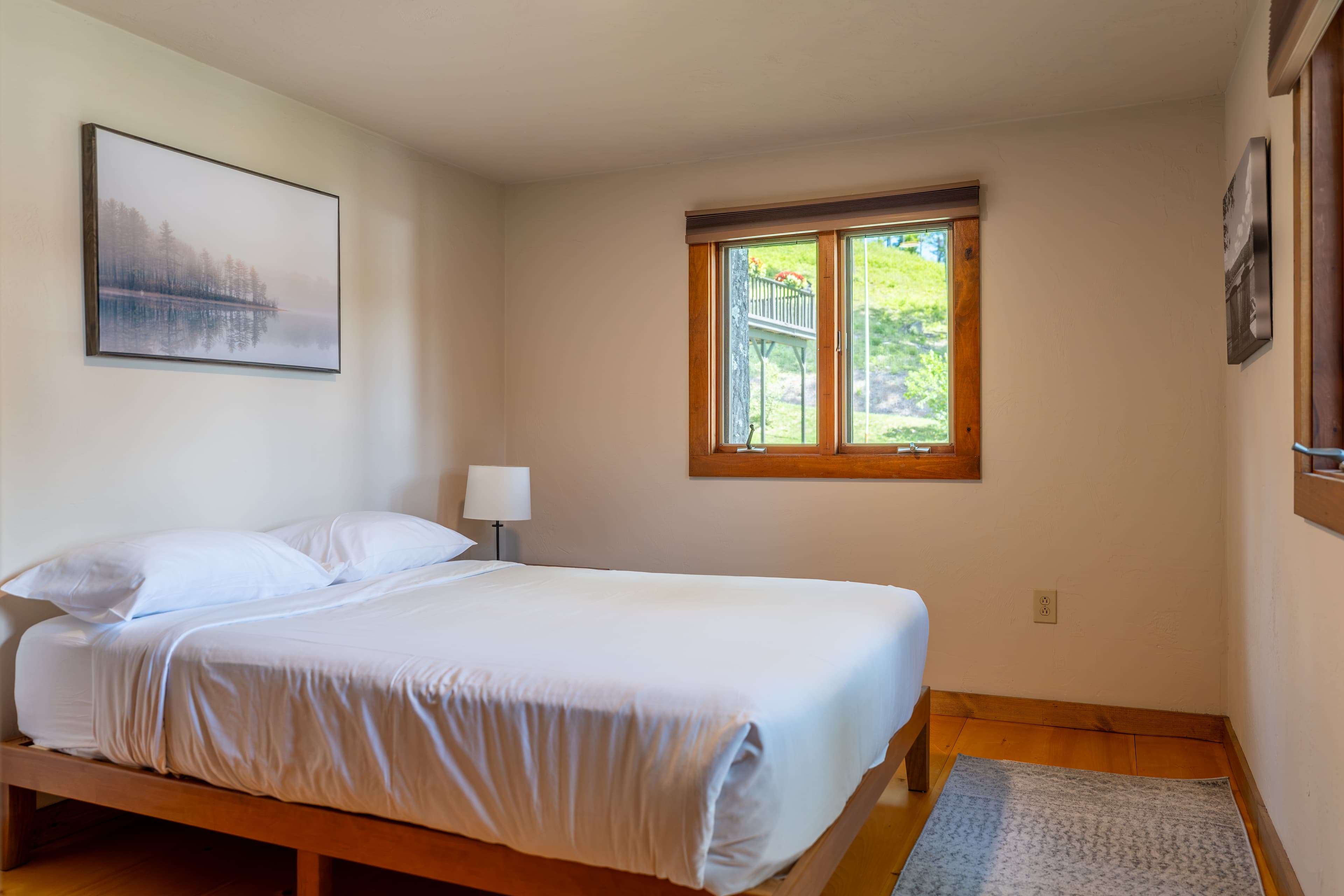 A cozy bedroom with a double bed covered by a patterned quilt, framed by two matching lamps on wooden nightstands and a small window.