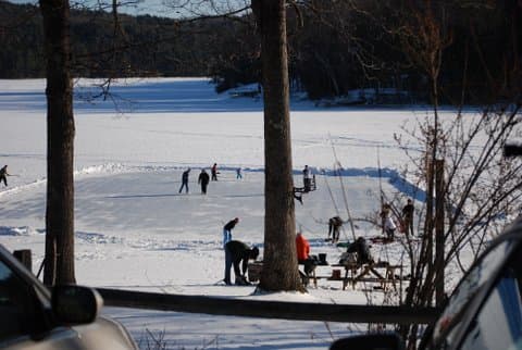People ice skating on a frozen lake surrounded by snow and trees.