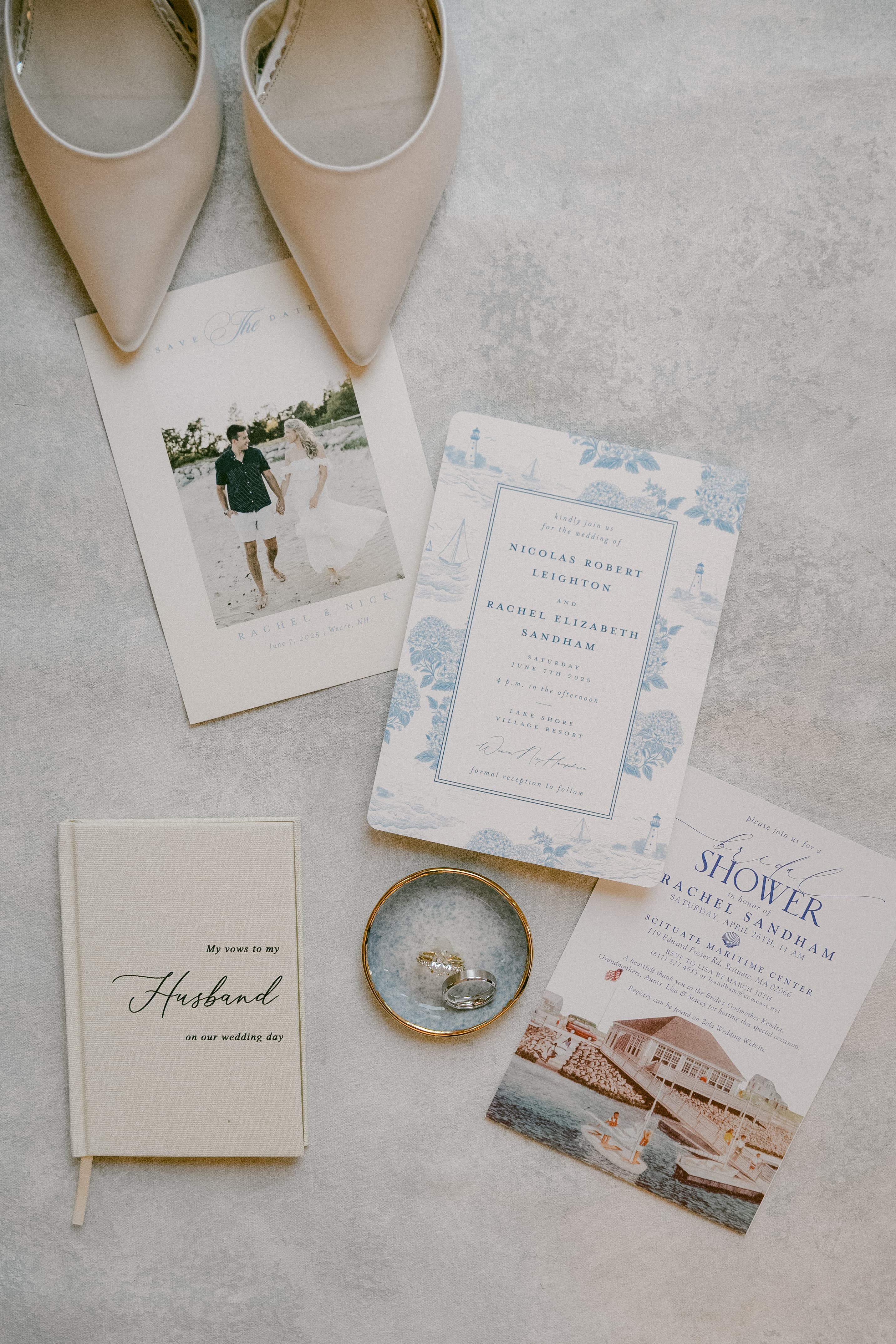 Arranged wedding memorabilia including shoes, invitations, a vow book, and rings on a gray surface.