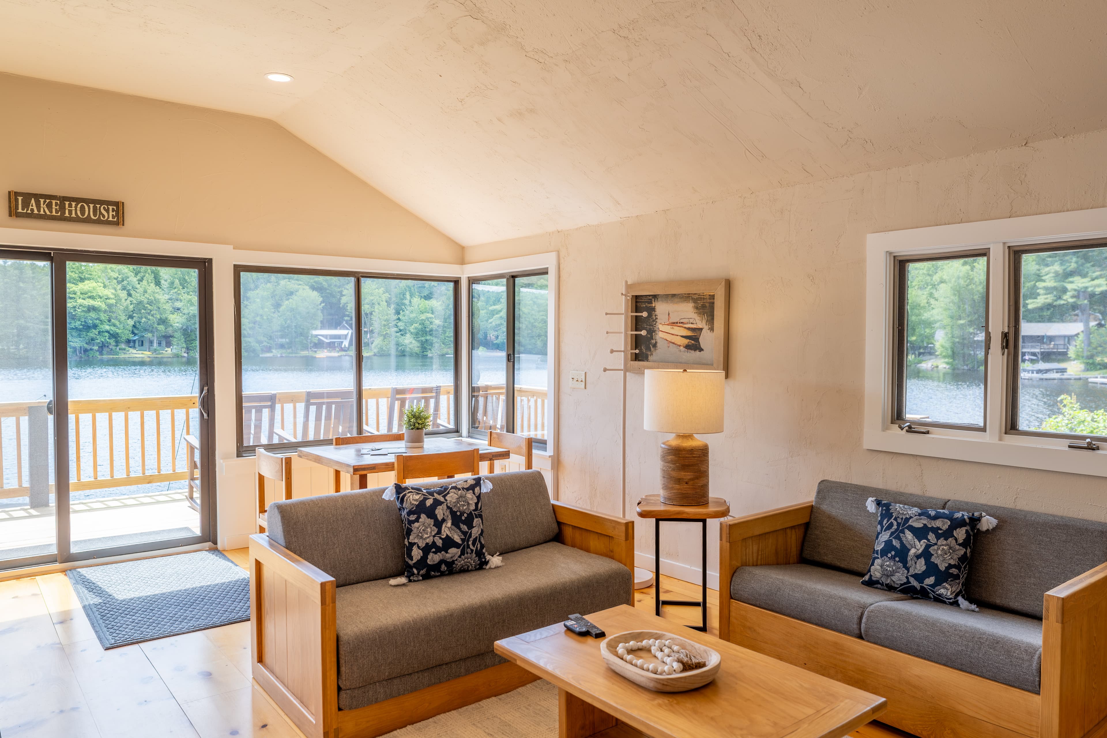 A rustic cabin living and dining area with a vaulted ceiling, wood furniture, and a view through large windows.