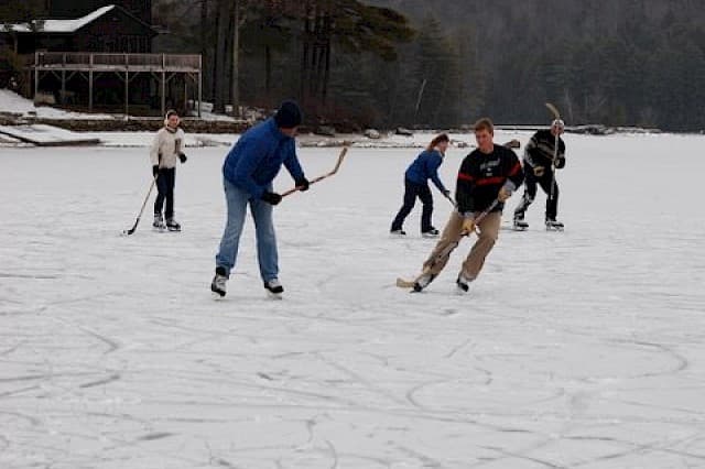 A group of people ice skating and playing hockey on a frozen lake.