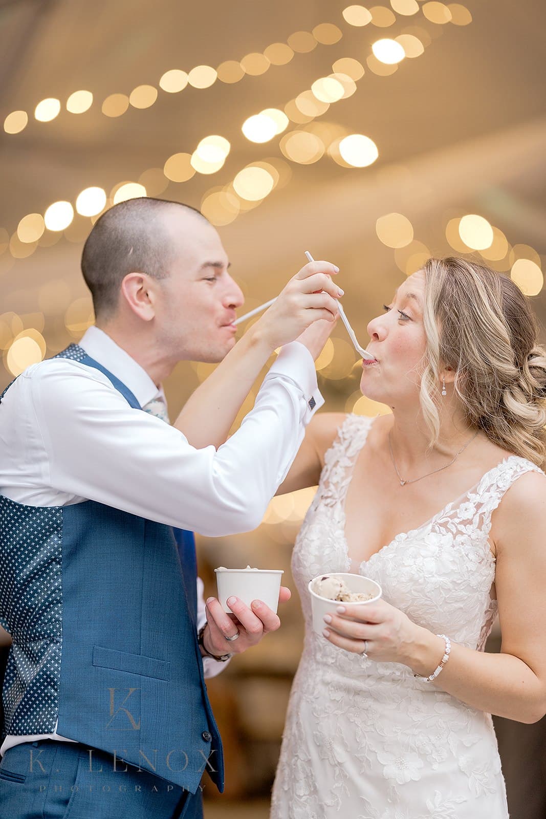 A couple playfully feeds each other ice cream at a celebration, surrounded by soft, warm lights.
