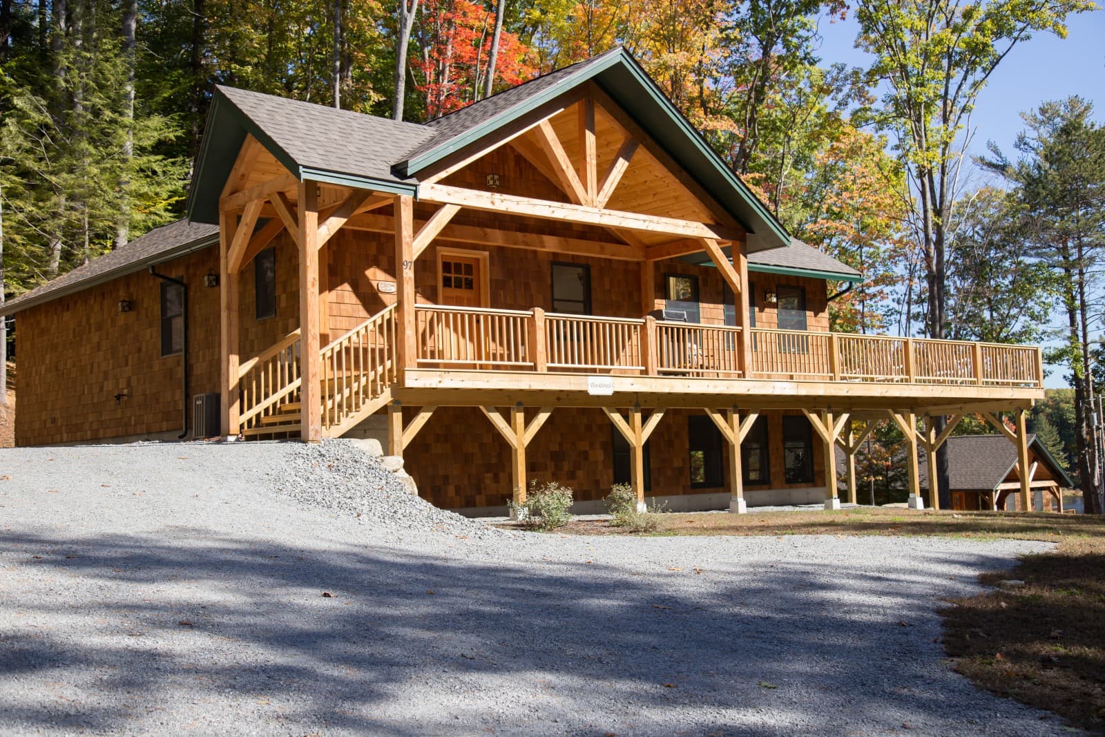 A wooden cabin with a spacious porch, surrounded by trees with autumn foliage.