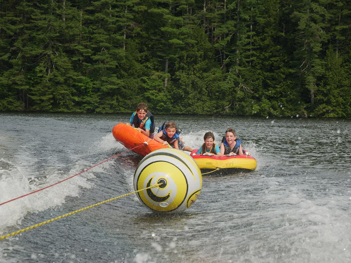 Four children are enjoying tubing on a lake behind a motorboat.